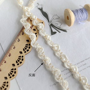 May include: White beaded trim with a gold thread design. The trim is shown on a wooden ruler with a scalloped edge. The text "反面" is visible on the image.