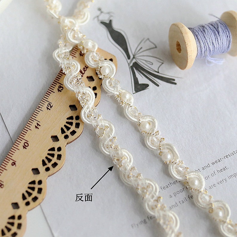 May include: White beaded trim with a gold thread design. The trim is shown on a wooden ruler with a scalloped edge. The text "反面" is visible on the image.