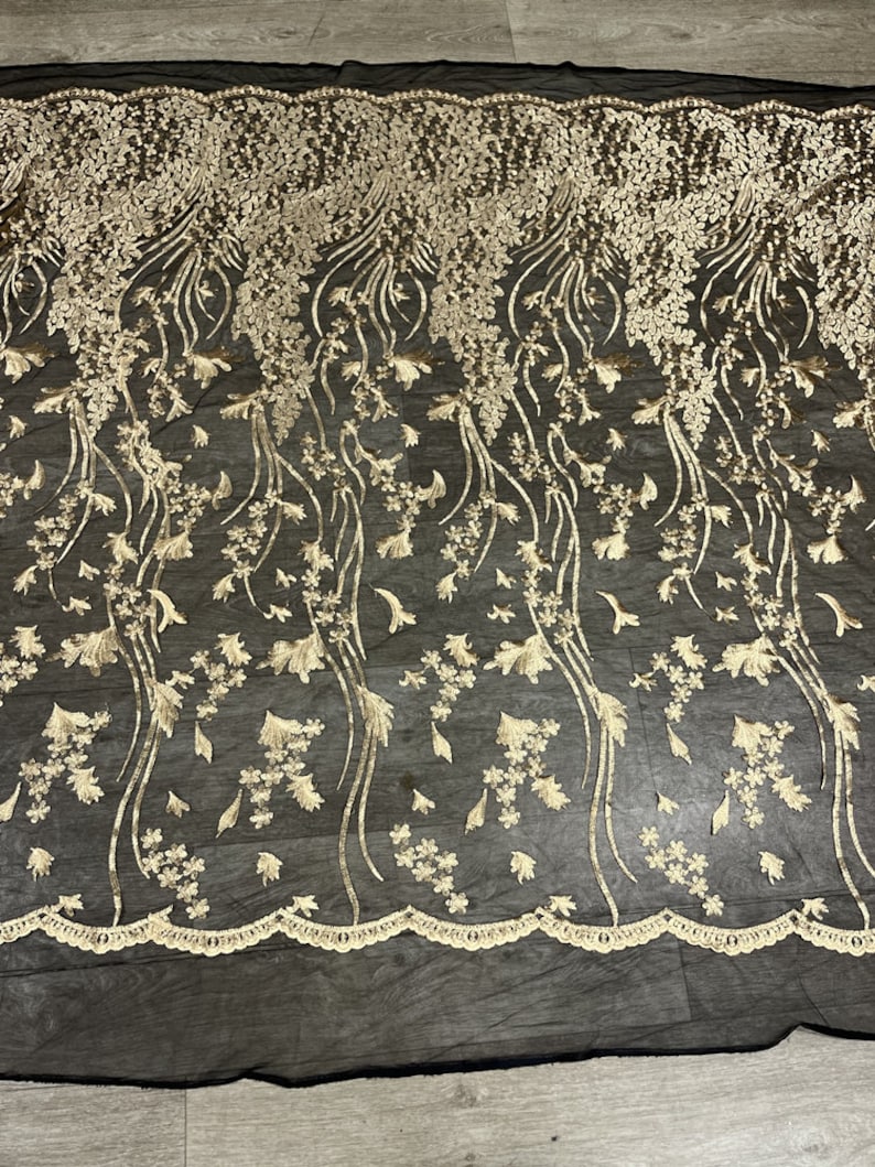 May include: Black mesh fabric with gold floral embroidery. The embroidery features delicate flowers and leaves, creating a flowing, elegant design.