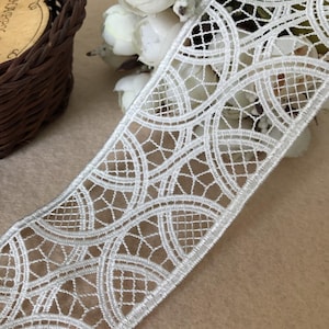 May include: White lace trim with a circular pattern. The lace is delicate and intricate, with a subtle shimmer.