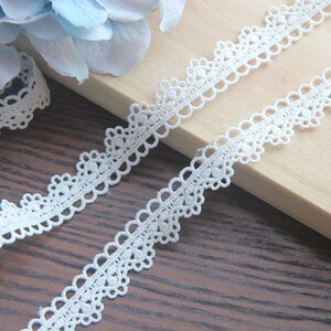May include: White lace trim with a delicate scalloped edge. The trim features a repeating pattern of small circles and ovals.