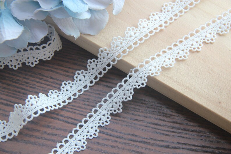 May include: White lace trim with a delicate scalloped edge. The trim features a repeating pattern of small circles and ovals.