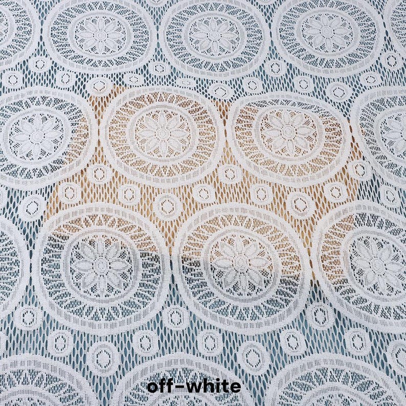 Peut inclure: Un tissu en dentelle blanc cass&eacute; pr&eacute;sentant un motif r&eacute;p&eacute;titif de grands cercles. Chaque cercle contient un dessin floral central entour&eacute; d'anneaux concentriques aux d&eacute;tails g&eacute;om&eacute;triques complexes, reli&eacute;s par un fond en maille fine.
