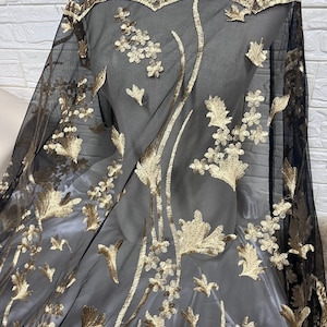 May include: Black sheer fabric with gold floral embroidery. The embroidery features delicate leaves and flowers.