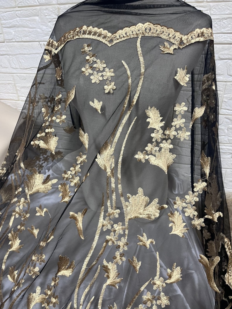 May include: Black sheer fabric with gold floral embroidery. The embroidery features delicate leaves and flowers.