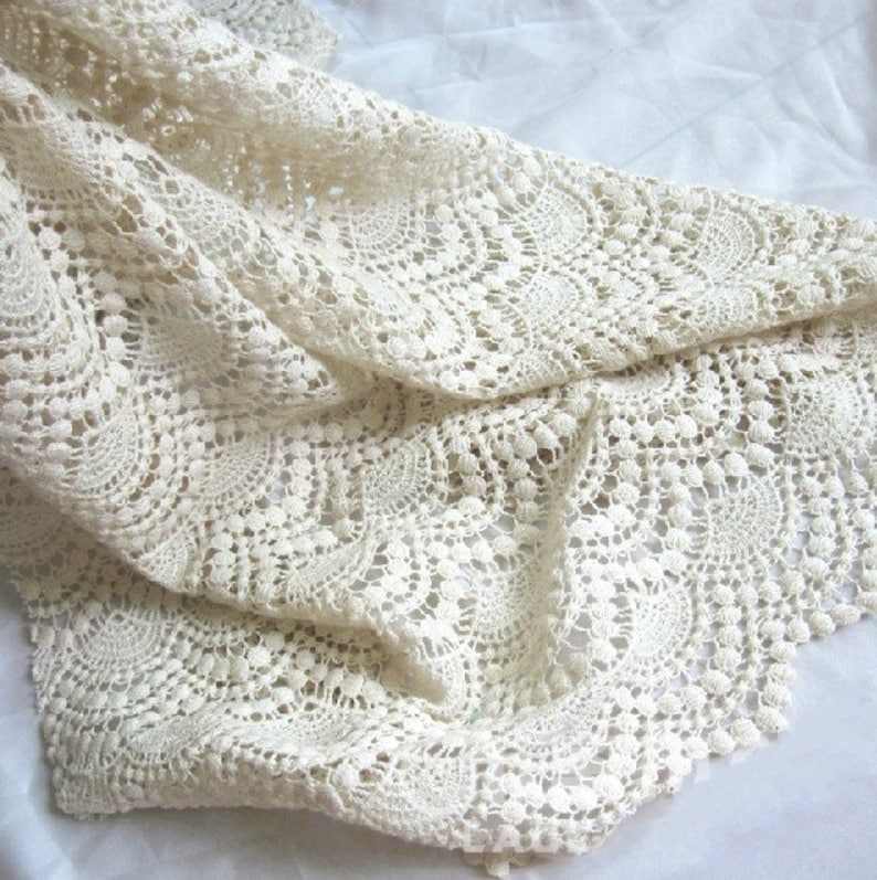 May include: Cream-colored crocheted lace fabric with a delicate pattern of circles and scallops. The fabric is soft and lightweight, making it ideal for a variety of crafting projects.