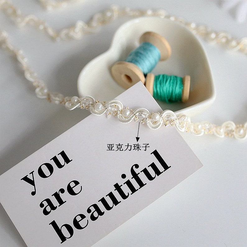 May include: White beaded trim with a scalloped edge. The trim is on a white surface with a card that says "you are beautiful".