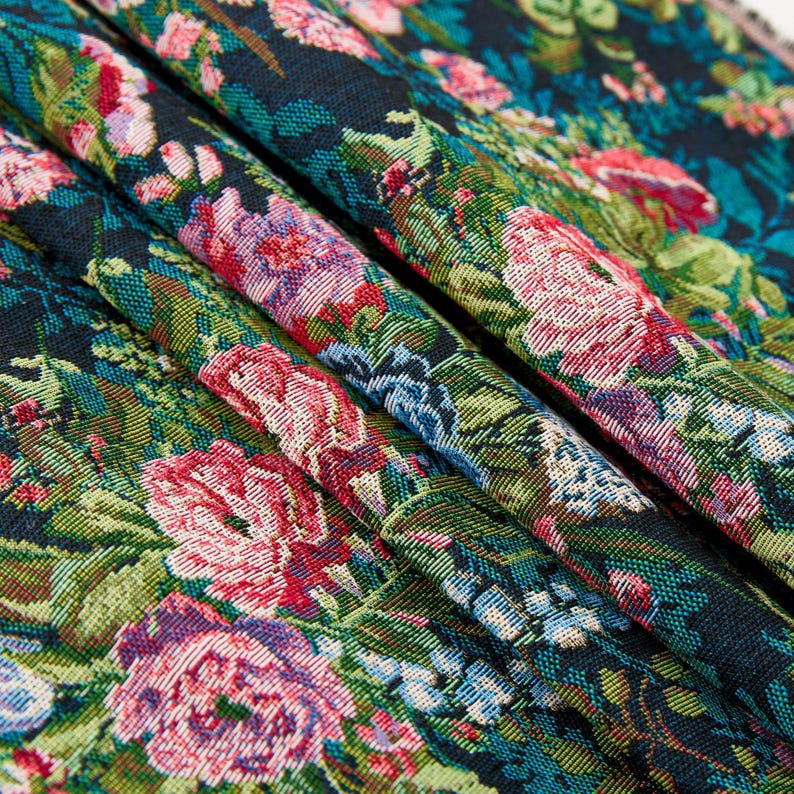 Puede incluir: Una tela tejida con un denso patr&oacute;n floral de flores de color rosa vibrante, rojo y azul claro sobre un fondo negro oscuro. El tejido muestra un intrincado follaje y hojas verdes, creando un dise&ntilde;o bot&aacute;nico texturizado y multicolor.