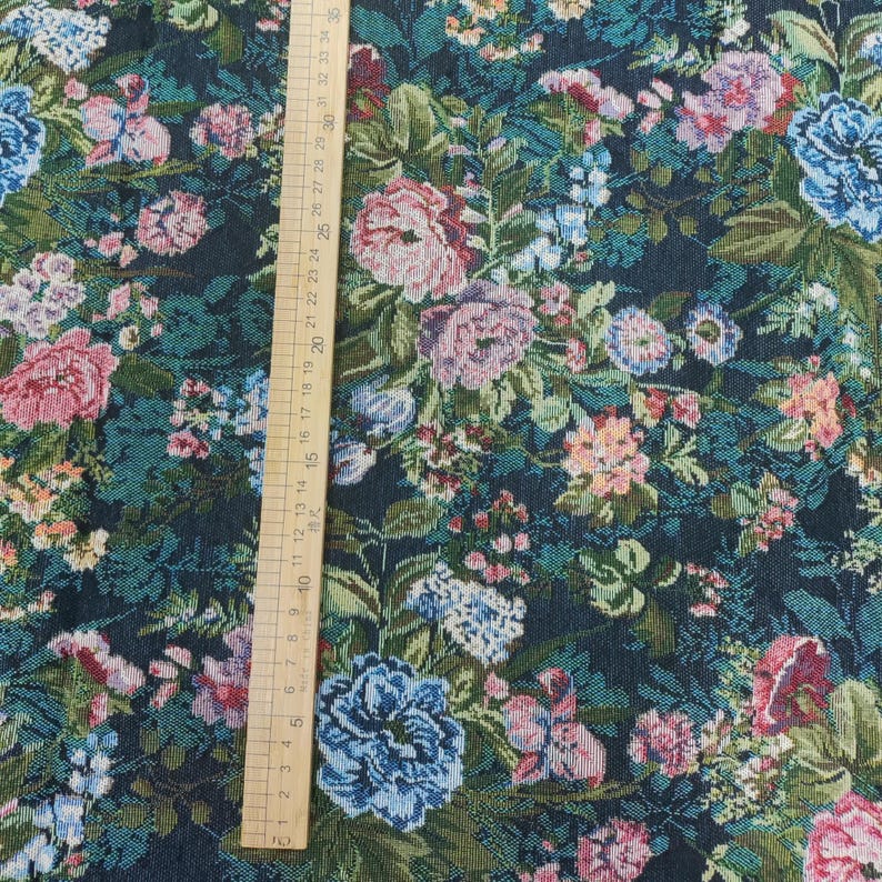 Puede incluir: Una tela oscura con un denso patr&oacute;n floral de flores y hojas rosas, azules y verdes. Una regla de madera est&aacute; colocada verticalmente en el lado izquierdo, mostrando medidas en cent&iacute;metros hasta 35 cm, proporcionando una escala clara del dise&ntilde;o.