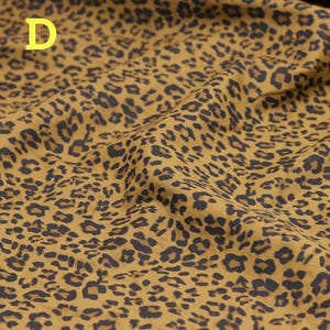May include: Mustard-colored fabric with a leopard print pattern. The fabric has a repeating design of dark brown spots on a tan background. The letter "D" is in the upper left corner of the image.