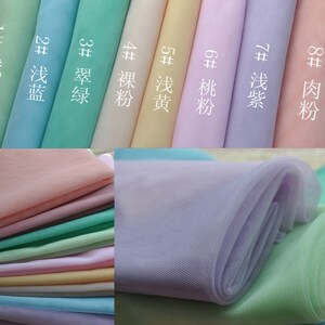 May include: A close-up of ten different colors of sheer tulle fabric. The colors are: light green, light blue, teal, cream, light yellow, light pink, lavender, and peach. The fabric is arranged in a row, with the colors labeled in Chinese characters.