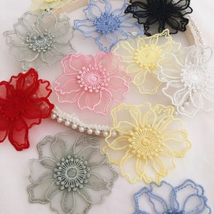 May include: A collection of multi-colored floral lace appliques in shades of red, pink, yellow, white, blue, gray, and black. Each flower features intricate embroidered petals and a detailed center, arranged on a circular mesh frame.