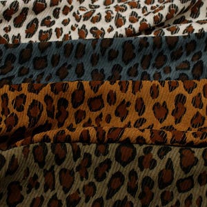 Puede incluir: Primer plano de varias muestras de tela con un diseño de estampado de leopardo. Las telas son de varios colores, incluyendo crema, azul grisáceo, marrón dorado y verde oliva. Las manchas de leopardo son marrones y negras.