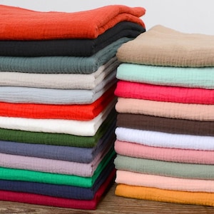 Puede incluir: Montones de tela doblada en varios colores, incluyendo rojo, negro, verde, gris y azul. La tela tiene una apariencia texturizada, y las pilas están cuidadosamente dispuestas, mostrando una gama de tonos adecuados para proyectos textiles.