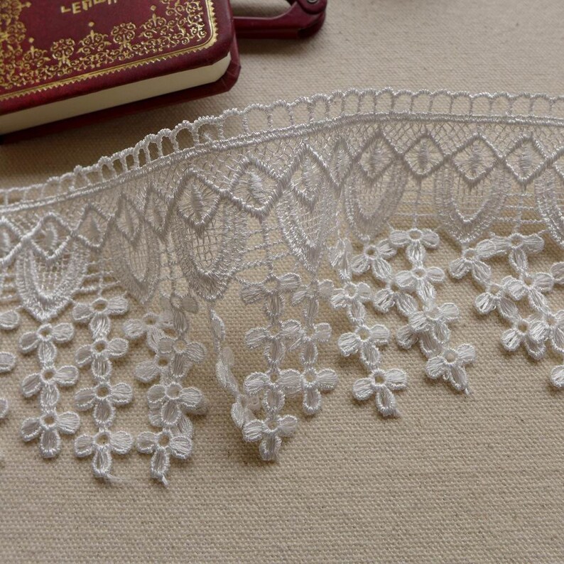 May include: White lace trim with a scalloped edge and a delicate floral pattern. The lace has a fringe of small flowers.