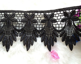 May include: Black lace trim with a delicate floral design. The trim features a scalloped edge and a repeating pattern of flowers and leaves.