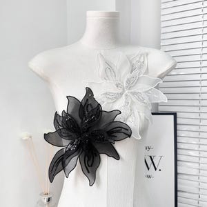 May include: Two black and white floral appliques with beaded details. The appliques are made of sheer fabric and have a delicate, feminine look.