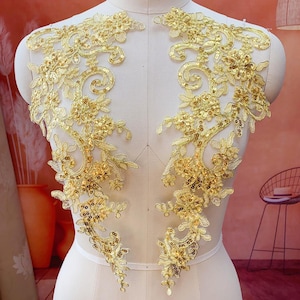 May include: Two golden lace appliques with floral and leaf designs. The appliques are embellished with sequins and are displayed on a mannequin. The lace has a delicate, intricate pattern, perfect for embellishing garments or crafts.