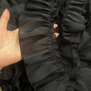 Puede incluir: Tela negra transparente con múltiples capas de volantes. La tela es suave y delicada, con una superficie ligeramente texturizada.