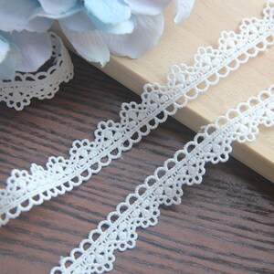 May include: White lace trim with a delicate scalloped edge. The trim is made of a fine, lightweight material and has a delicate, feminine look.