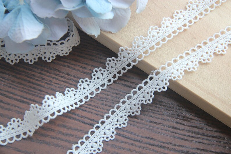 May include: White lace trim with a delicate scalloped edge. The trim is made of a fine, lightweight material and has a delicate, feminine look.