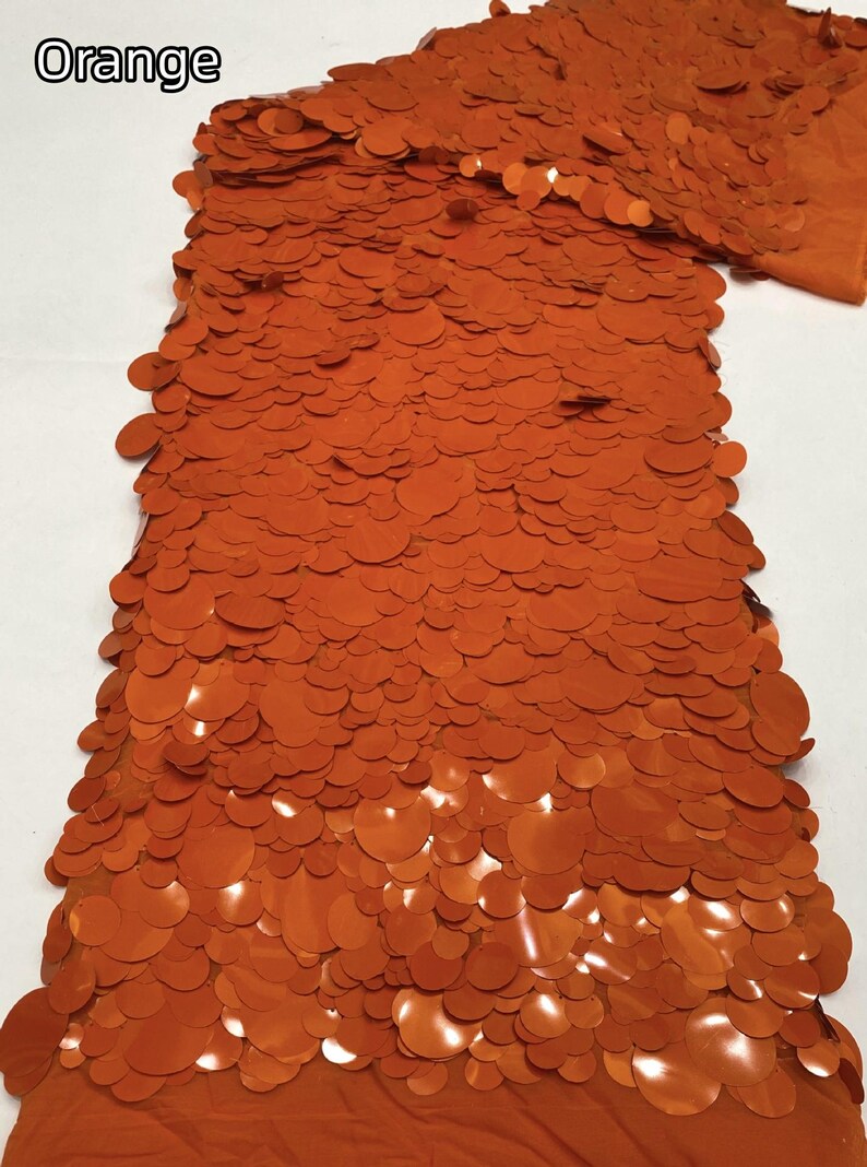 Puede incluir: Una muestra de tela de color naranja vibrante, densamente cubierta con lentejuelas circulares superpuestas de varios tama&ntilde;os. Las lentejuelas est&aacute;n unidas a una tela base naranja a juego, creando una superficie texturizada y reflectante con la palabra Orange.