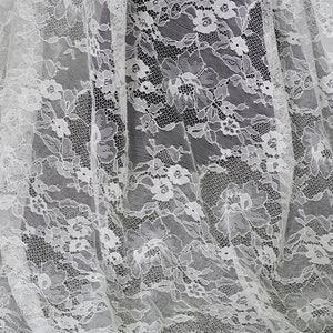 Puede incluir: Tela de encaje blanca con un delicado patrón floral. El encaje es transparente y tiene una textura suave y fluida.