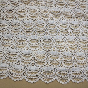 May include: White crochet fabric with a scalloped pattern. The fabric has a delicate, lacy texture.