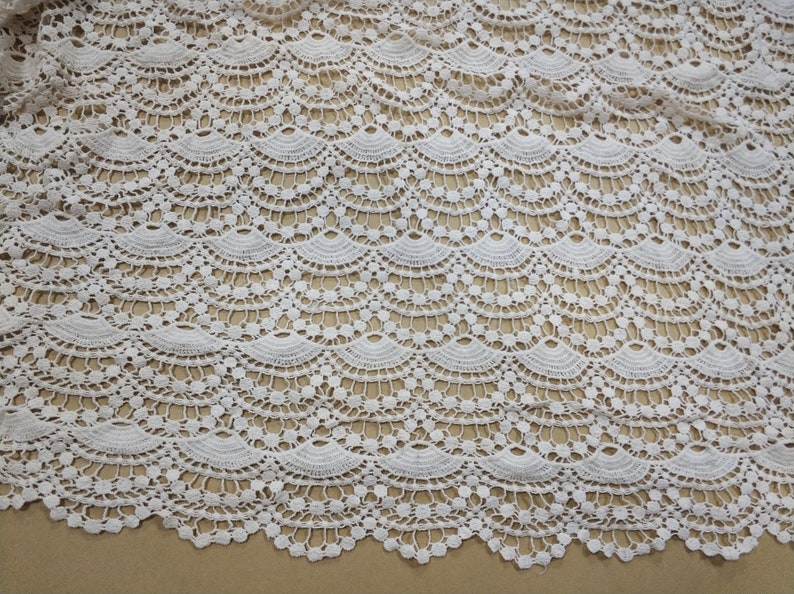 May include: White crochet fabric with a scalloped pattern. The fabric has a delicate, lacy texture.
