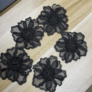 May include: Four black floral appliques made of sheer mesh fabric with intricate embroidery. Each piece features a central circular design with radiating petals and scalloped edges, showcasing a delicate, semi-transparent layered construction.