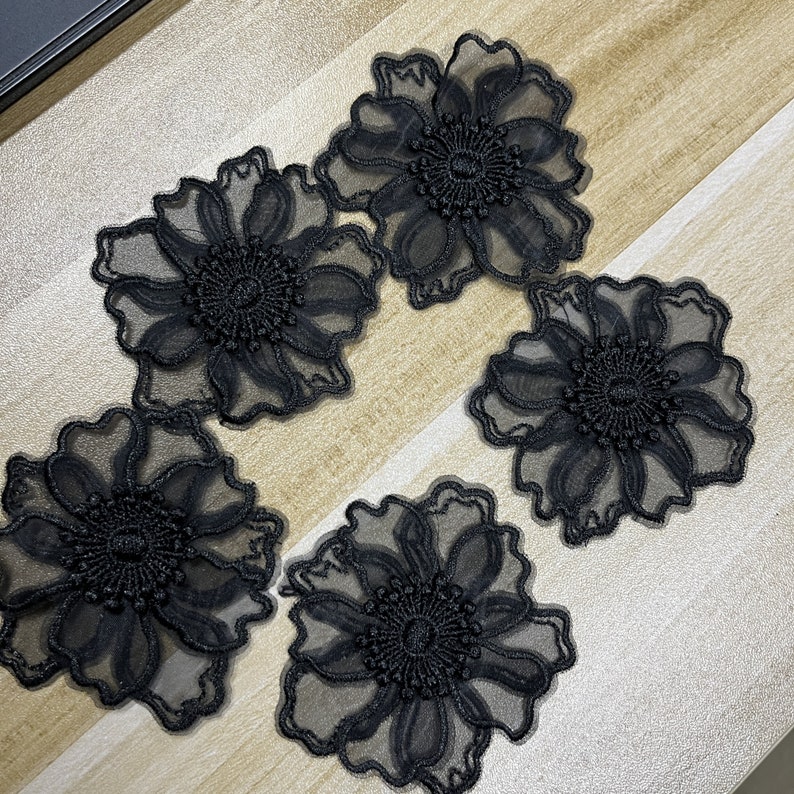 May include: Four black floral appliques made of sheer mesh fabric with intricate embroidery. Each piece features a central circular design with radiating petals and scalloped edges, showcasing a delicate, semi-transparent layered construction.