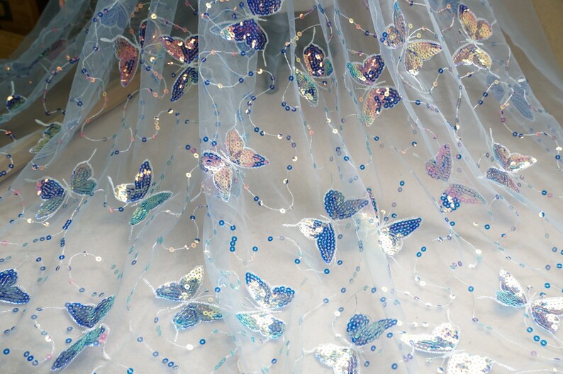 May include: Light blue tulle fabric with iridescent butterfly sequins. The fabric is sheer and has a delicate, feminine feel.