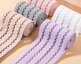 May include: Five rolls of elastic fabric trim in pastel pink, gray, peach, lavender, and white. Each roll features a repeating openwork pattern with vertical woven bands and a series of small triangular cutouts running along the length of the material.