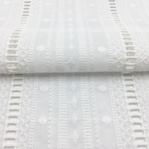 May include: White cotton fabric with embroidered vertical stripes of different patterns. The fabric has a delicate, lacy look.