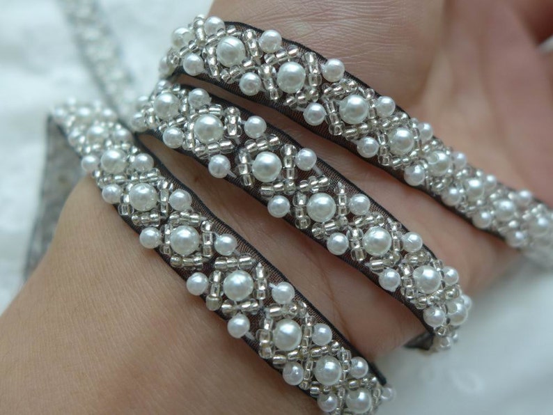 May include: White pearl trim with silver beads on black mesh ribbon.