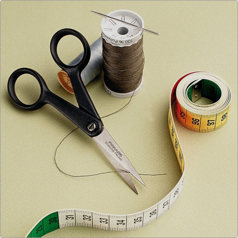 May include: Black fabric scissors with a silver blade and a brown spool of thread with a needle. A white measuring tape with black numbers is curled around the spool of thread and scissors.