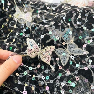 May include: Black mesh fabric with iridescent sequins and embroidered butterflies. The butterflies are in shades of pink, white, and silver.