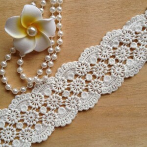 May include: White crochet lace trim with a delicate floral pattern. The lace is about 1 inch wide and has a scalloped edge.