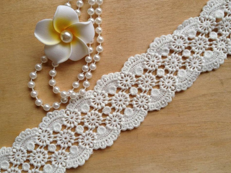 May include: White crochet lace trim with a delicate floral pattern. The lace is about 1 inch wide and has a scalloped edge.