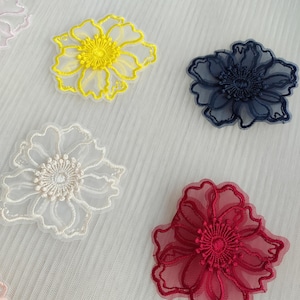May include: Four floral appliques made of sheer organza fabric with intricate embroidery. The set includes one bright yellow flower, one dark navy blue flower, one off-white flower, and one deep red flower, all featuring detailed centers.