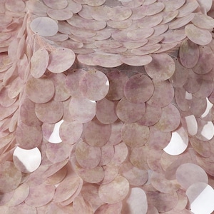 May include: A textile fabric featuring a dense layer of overlapping, circular, pale pink sequins with a subtle mottled texture. The sequins are attached to a fine, translucent mesh base, creating a layered, scale-like appearance across the surface.