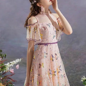 May include: A pink off-the-shoulder dress with butterfly sequins. The dress has a ruffled neckline and short sleeves.