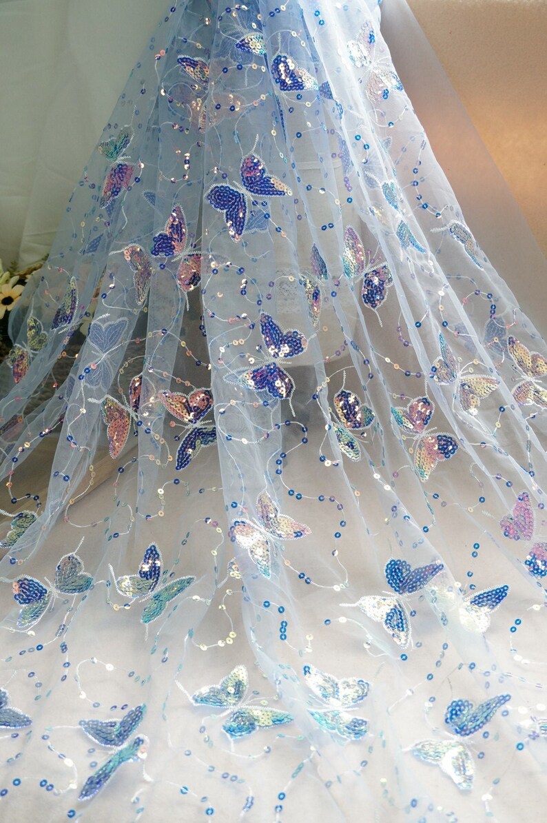 May include: Light blue sheer fabric with iridescent butterfly sequins. The fabric is delicate and has a soft, flowing texture.