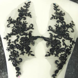 May include: A pair of black lace appliqués featuring intricate floral embroidery and black bead embellishments on a sheer mesh base. The symmetrical design showcases detailed vine and petal patterns, crafted with dark thread and glossy black beads.