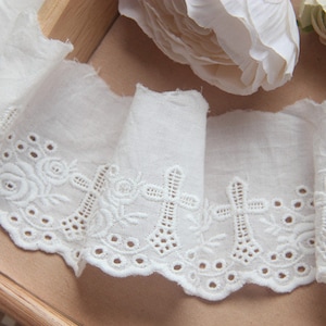 May include: White cotton lace trim with a scalloped edge and embroidered cross and floral designs.