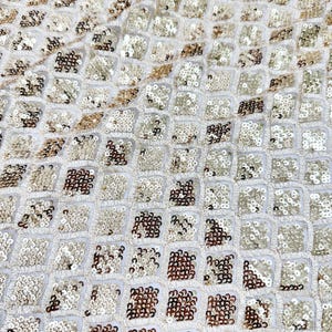 May include: A fabric textile featuring a repeating geometric diamond pattern. The design consists of small, shimmering gold and bronze sequins densely embroidered onto a sheer, off-white mesh base, creating a textured and reflective surface.