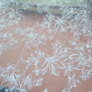 Könnte beinhalten: Hellpfirsichfarbener, transparenter Stoff mit weißem Blumenmuster. Das Design zeigt große, detaillierte Blumen mit einer zarten, handgezeichneten Ästhetik. Dieser Stoff eignet sich für Kleidung oder Heimdekoration.