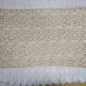 May include: Beige lace fabric with a scalloped pattern. The lace has a delicate, intricate design with small holes throughout.
