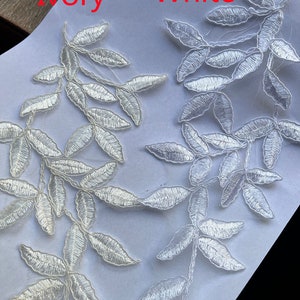 May include: Two samples of lace trim, one in ivory and one in white. Both trims feature a delicate leafy design.