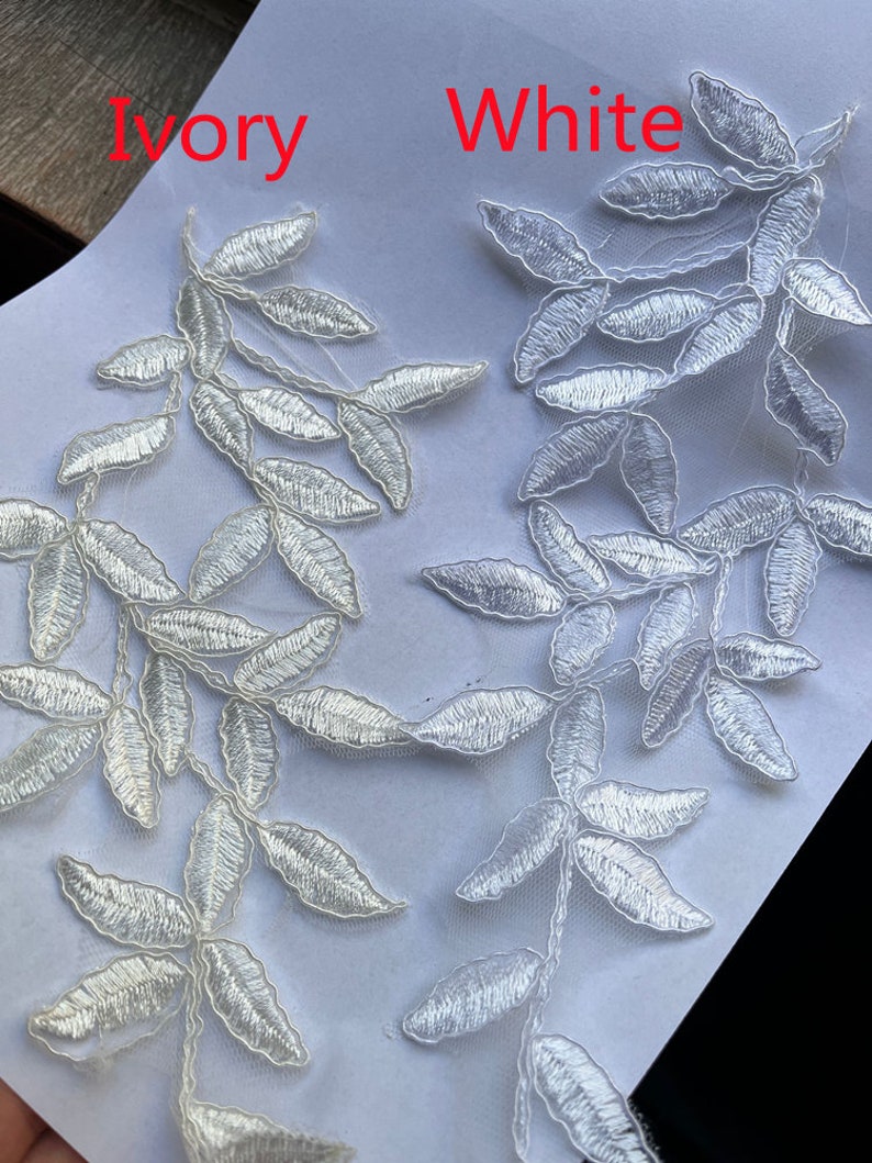 May include: Two samples of lace trim, one in ivory and one in white. Both trims feature a delicate leafy design.